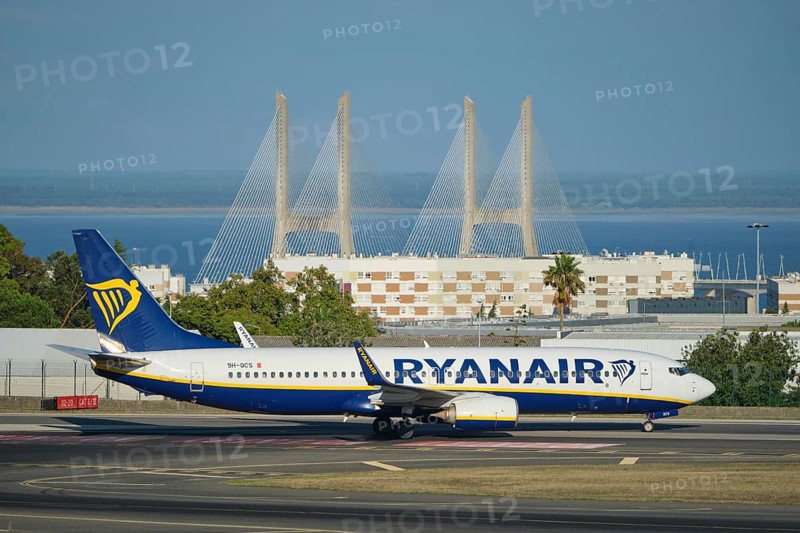 Lisbon, Portugal - September 2, 2023: Ryanair Boeing 737-8AS passenger plane taxi on runway in Humberto Delgado Airport in Lisbon with Vasco da Gamma bridge in background