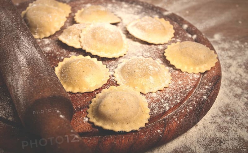 Fresh raw, uncooked ravioli, on a cutting board, with a rolling pin for dough, wooden background, no people
