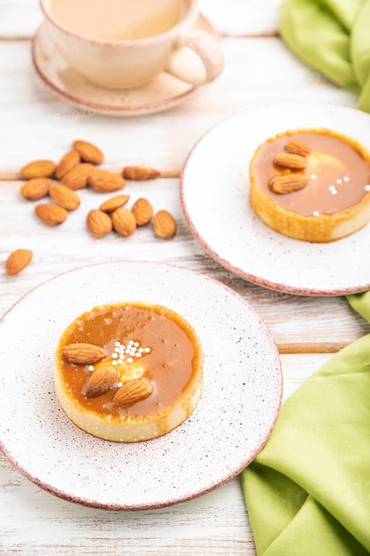 Sweet tartlets with almonds and caramel cream with cup of coffee on a white wooden background and green textile. side view, close up, selective focus