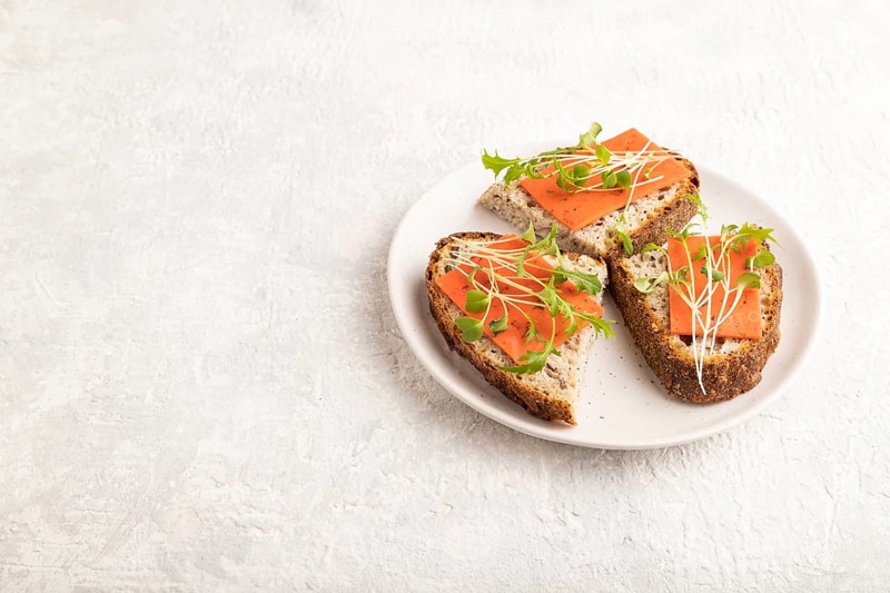 Grain bread sandwiches with red tomato cheese and mizuna cabbage microgreen on gray concrete background. side view, copy space