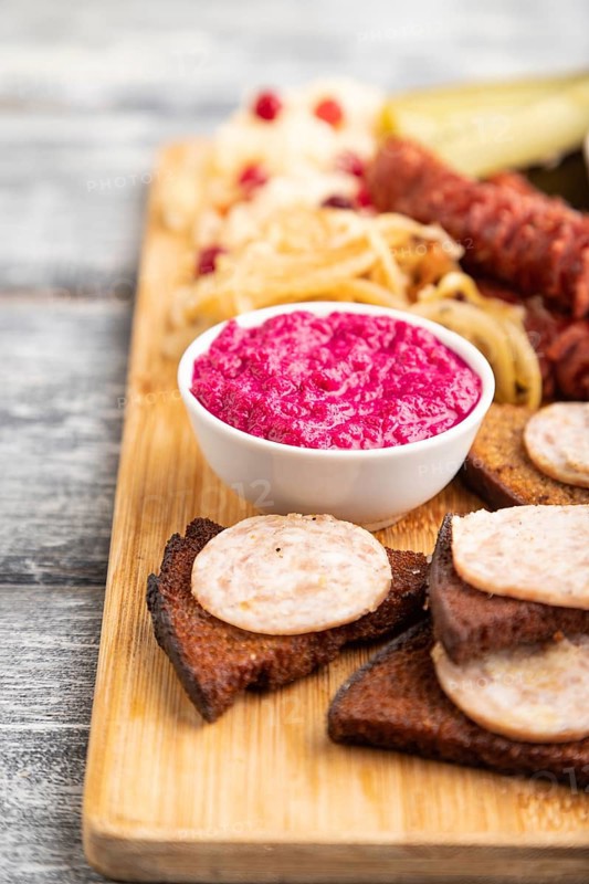 Set of snacks: sausages, toast, sauerkraut, marinated onion and cucumber, baked potato on a cutting board on a gray wooden background. Side view, close up, selective focus