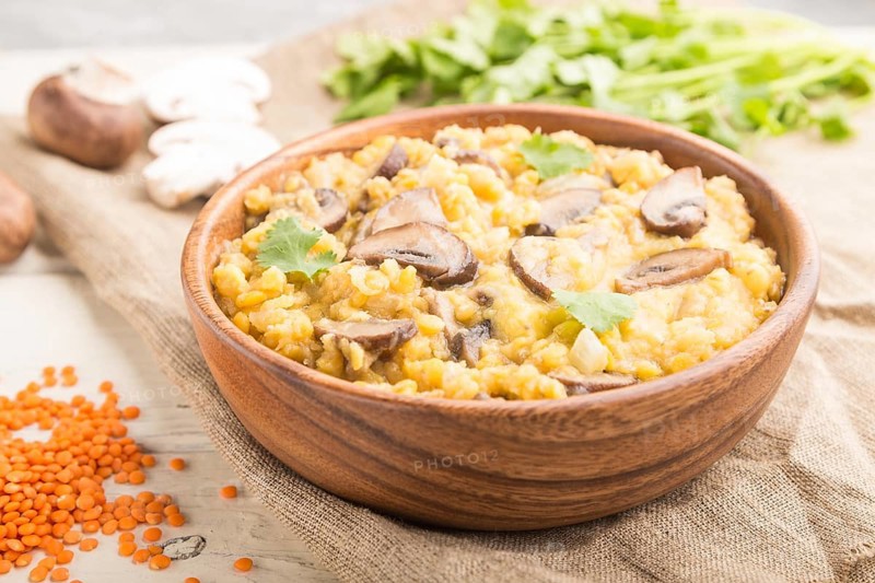 Lentils porridge with champignons and coriander in a wooden bowl on a white wooden background and linen textile. Side view, close up, selective focus