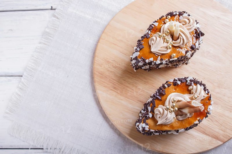 Cakes with chocolate chips and cream decorations on wooden board on white background. selective focus, close up, copy space