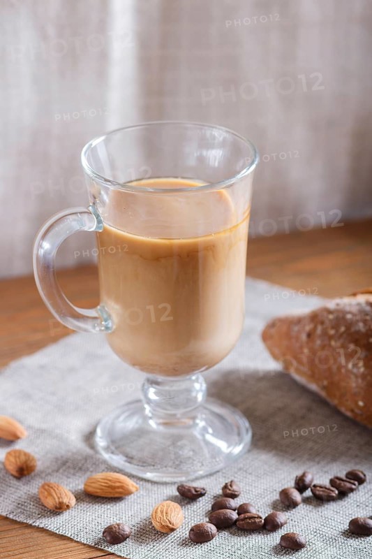 Glass cup of coffee with cream and bun on a wooden background and linen textile. close up
