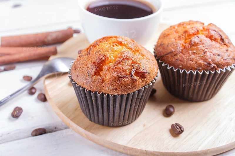 Two carrot muffins with cup of coffee on wooden kitchen board on white wooden background with cinnamon and spoon. closeup