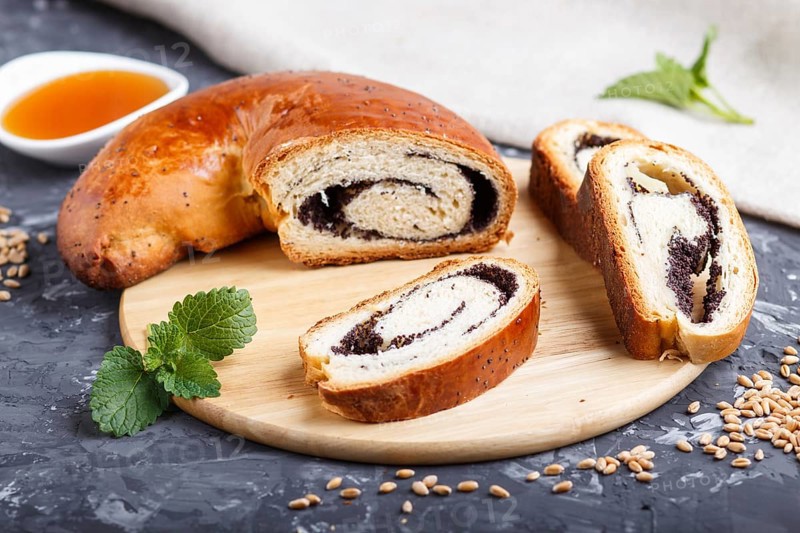 Homemade yeast rolls with poppy seeds and honey on a wooden kitchen board on a black concrete background. side view. close up, selective focus