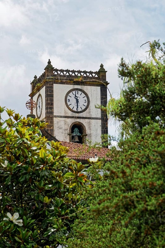 An old church tower Câmara Municipal de Vila Franca do Campo with a large clock and bell, surrounded by green trees and a cloudy sky, small town Vila Franca do Campo, Sao Miguel, Azores, Portugal, Europe