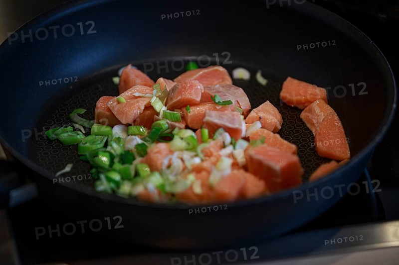 Fry the fresh salmon pieces and chopped spring onions in a black pan on the hob
