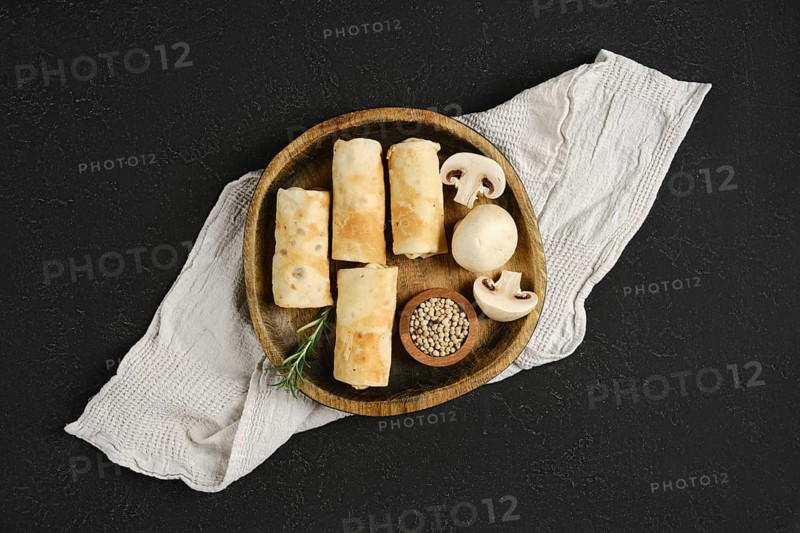 Thin pancakes stuffed with mushrooms on a wooden plate. The rustic setting enhances the appetizing arrangement of food and ingredients.