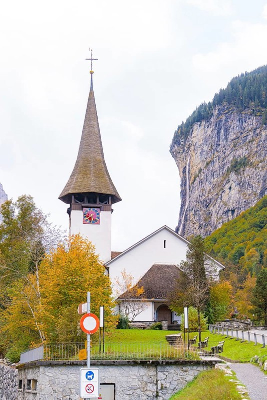 Church with pointed tower in front of rock face and waterfall in an autumn landscape, Lauterbrunnen, Switzerland, Europe