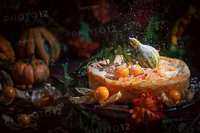 Icing sugar falls on autumnal cake with yellow physalis and pumpkin, romantic atmosphere