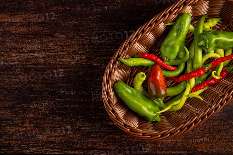 A brown basket with green and red peppers on a wooden base