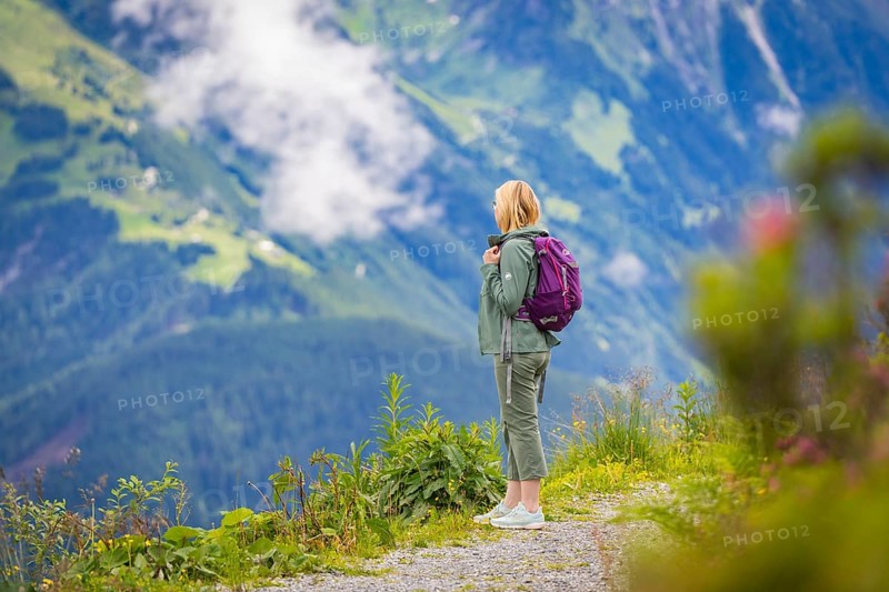 Woman on a hiking trail against a breathtaking mountain backdrop with flowering plants in the foreground, Penken, Zillertal. Austria