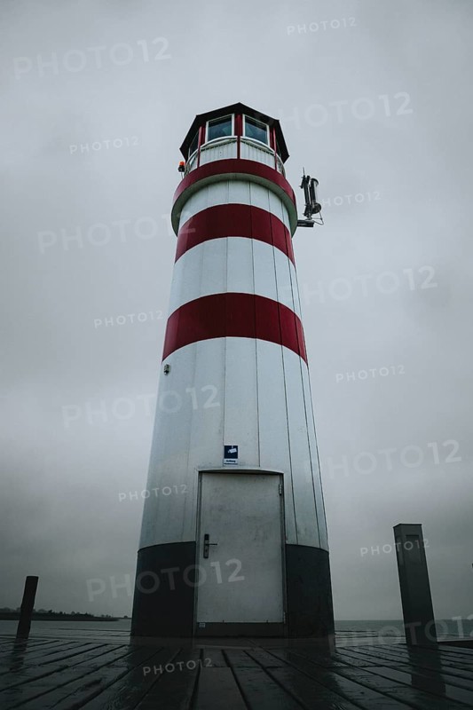 A red and white lighthouse stands on a wooden plank under a grey sky, Podersdorf, Burgenland, Austria, Europe