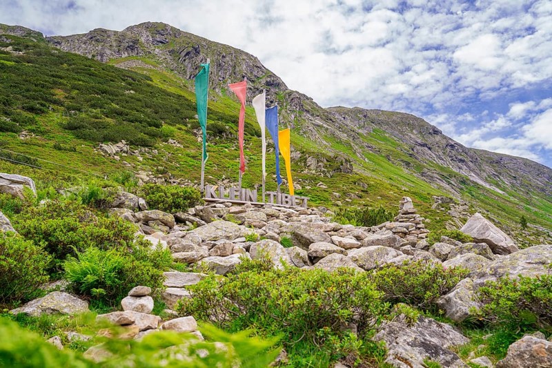 Landscape in the mountains with colourful flags, a sign and green vegetation, framed by rocks, Little Tibet, Zillertal, Austria, Europe