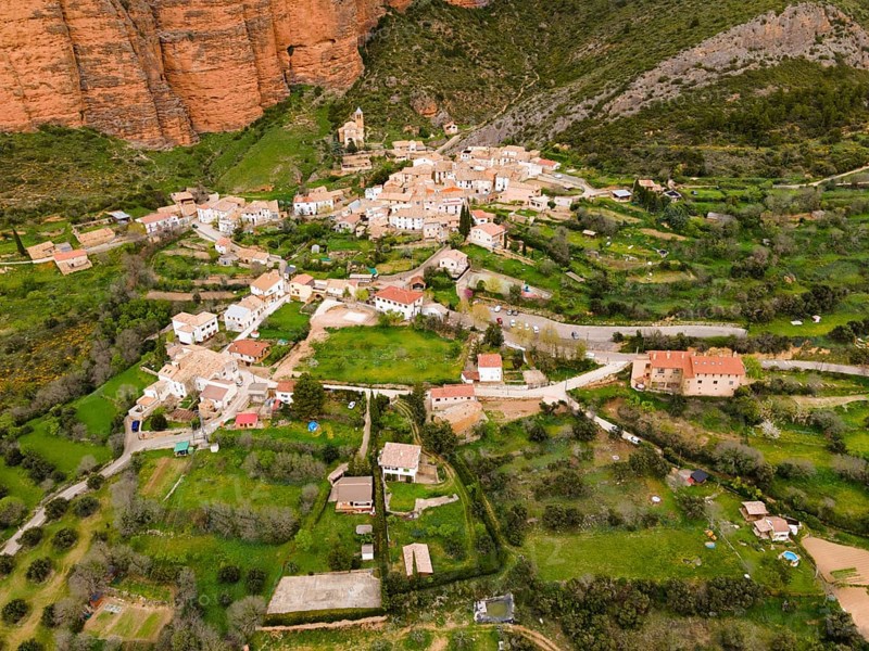Aerial view of a picturesque village surrounded by green hills and striking orange rocks, aerial view, Las Peñas de Riglos, As Penyas de Riglos, Mallos de Riglos rock formation, Huesca, Aragon, Spain, Europe