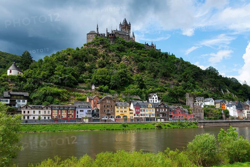 Image of a castle on a green hill with colourful, historic buildings along a river, cloudy sky, Reichsburg, Cochem, Cochem-Zell, Moselle, Rhineland-Palatinate, Germany, Europe