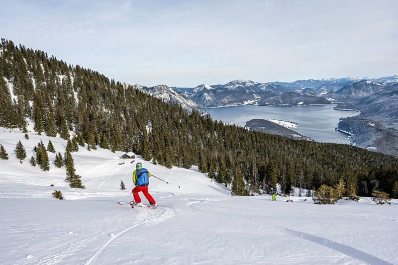Skiers skiing down the Simetsberg, view of Walchensee and mountain panorama, Estergebirge, Bavarian Prealps, Bavaria Germany