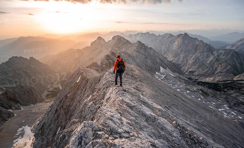 Mountaineer with helmet on a narrow rocky ridge at sunrise, crossing the Jubiläumsgrat, view of Höllental with Höllentalferner and Alpspitze, Wetterstein range, Bavaria, Germany, Europe