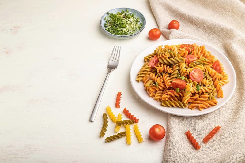 Tortiglioni semolina pasta with tomato and microgreen sprouts on a white wooden background and linen textile. Side view, copy space