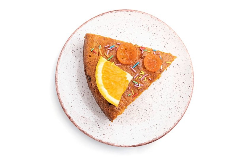 Piece of orange cake on ceramic plate isolated on a white background. Top view, close up
