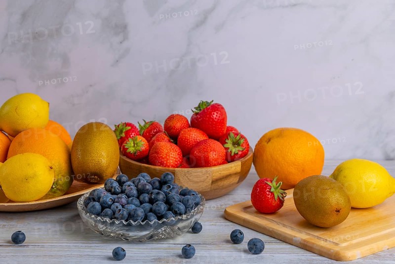 Harmonious still life of various fruits, strawberries, lemons, oranges, kiwis and blueberries on wood against a marble background