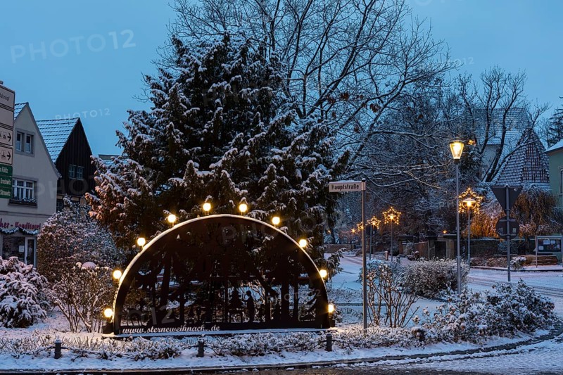 Candle arch on the main street, snow-covered and at dusk, in the background the old church, Coswig, Saxony, Germany, Europe