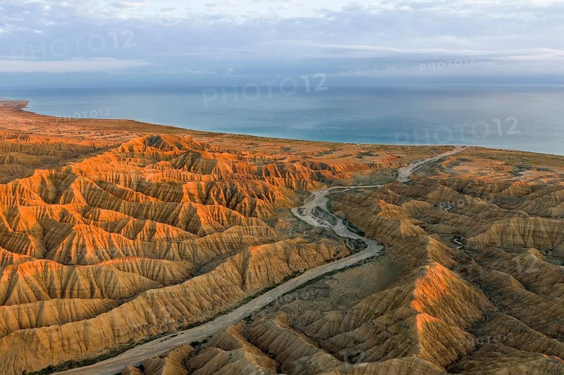 River bed runs through a landscape of eroded hills, badlands at sunset, Lake Issyk Kul in the background, aerial view, Canyon of the Forgotten Rivers, Issyk Kul, Kyrgyzstan, Asia