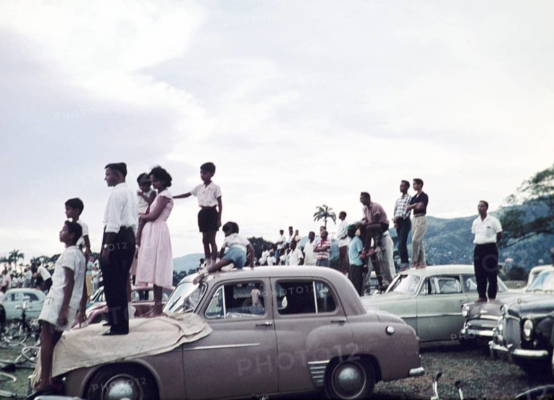 People standing on cars to watch a school sporting event - annual football match between Queen Mary's college and Queen's Royal college - Queen's Park Savannah, Port of Spain, Trinidad c 1962