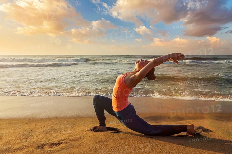 Yoga outdoors, sporty fit woman practices yoga Anjaneyasana, low crescent lunge pose outdoors at beach on sunset