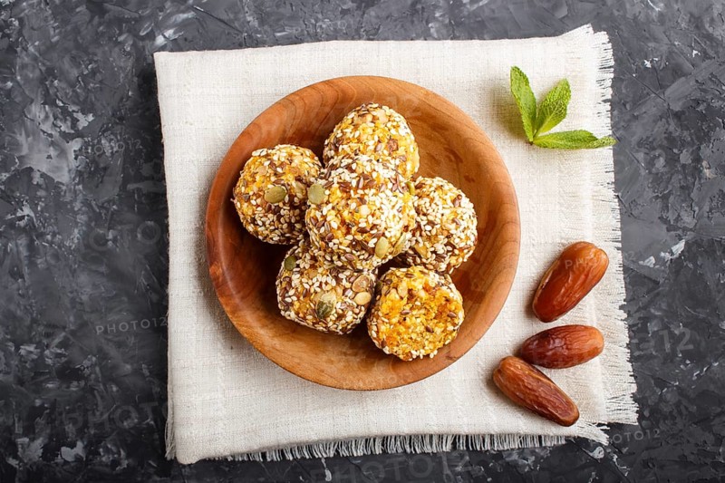 Energy ball cakes with dried apricots, sesame, linen, walnuts and dates with green mint leaves in a wooden bowl on a black concrete background. linen napkin, top view, close up, flat lay. vegan homemade candy
