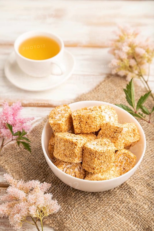 Traditional turkish delight (rahat lokum) in white ceramic plate with cup of green tea on a white wooden background. side view, close up