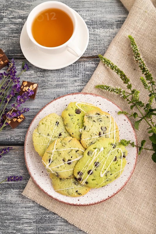 Green cookies with chocolate and mint on ceramic plate with cup of green tea and linen textile on gray wooden background. top view, flat lay, close up