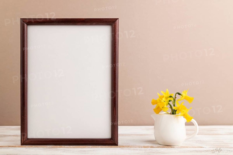 Wooden frame with spring snowdrop flowers narcissus on beige pastel background. side view, copy space, still life, mockup, template, spring minimalism concept
