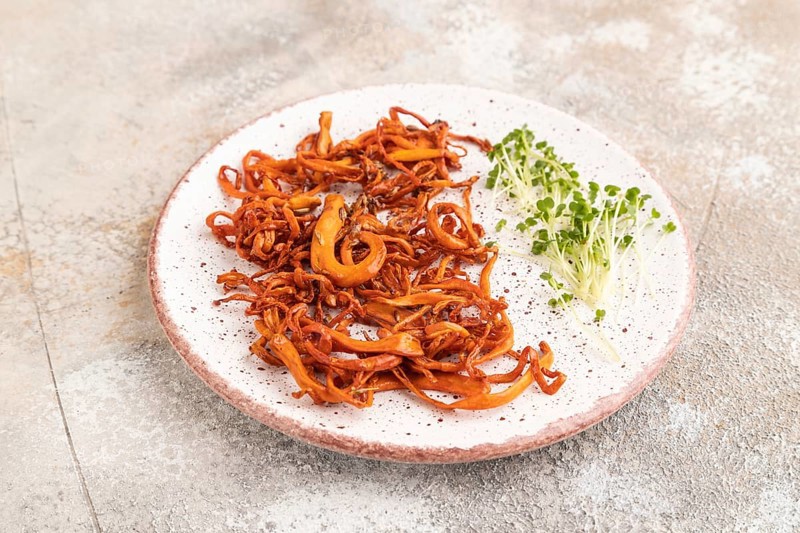Fried Cordyceps militaris mushrooms on brown concrete background with microgreen, herbs and spices. Side view, copy space