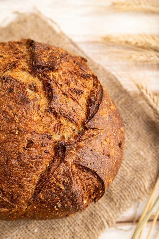 Fresh homemade golden grain bread with ears of wheat and rye on white wooden background and linen textile. side view, close up, selective focus