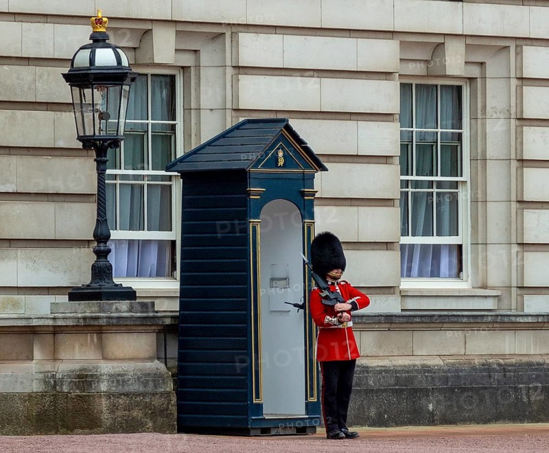 A guard in red uniform stands in front of a guardhouse next to a lantern at Buckingham Palace, London, United Kingdom United Kingdom