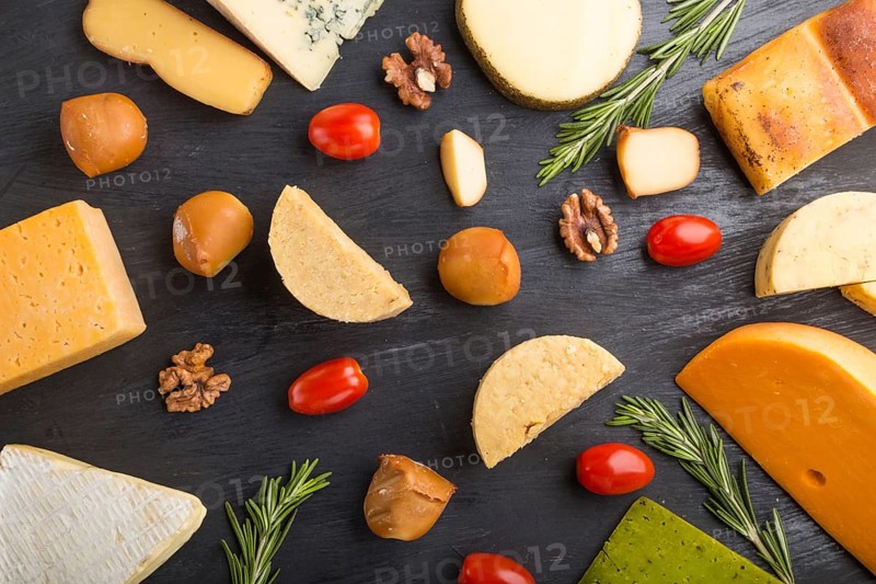 Set of different types of cheese with rosemary and tomatoes on a black wooden background. Top view, flat lay, close up