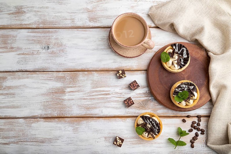 Sweet tartlets with chocolate and cheese cream with cup of coffee on a white wooden background and linen textile. top view, flat lay, copy space