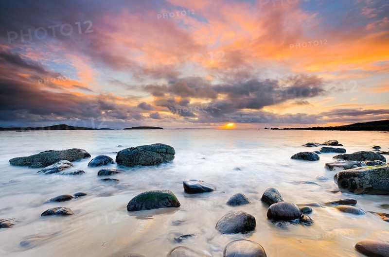 Orange coloured cloudy sky at sunset on a sandy beach strewn with round stones near Achiltibuie on the west coast of Scotland