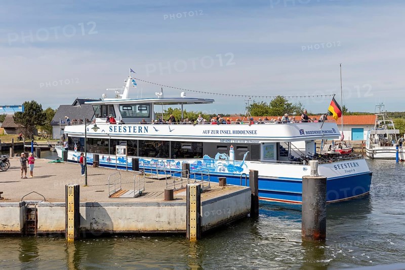 A large passenger ship with a flag is moored at the jetty in the sunny harbour, Rügen, Hiddensee