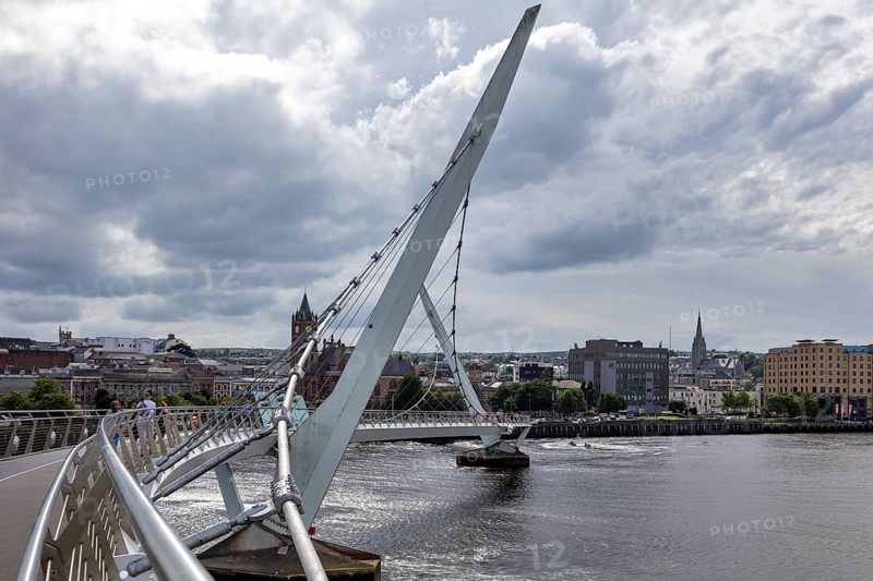 A deserted bridge over a tranquil river with dramatic clouds in the sky, Londonderry