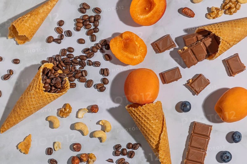 Ice cream cones with coffee beans, apricots, nuts and chocolate on a marble background