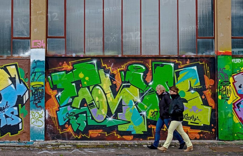 Two people walking along a wall covered with colourful graffiti, urban ambience, Landau, Rhineland-Palatinate, Germany, Europe