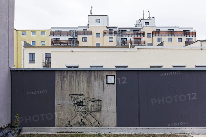 Shopping trolley with bricks instead of wheels, only preserved mural on a freshly painted wall, comsum-critical graffiti by street artist L.E.T., Düsseldorf, North Rhine-Westphalia, Germany, Europe