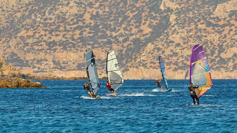 Windsurfers enjoy the sunny weather on the blue sea in front of a rocky coast, windsurfers, Meltemi windsurfing spot, Devils Bay, Paralia Vatha, Vatha Beach, south-east coast, Karpathos, Dodecanese, Greek Islands, Greece, Europe