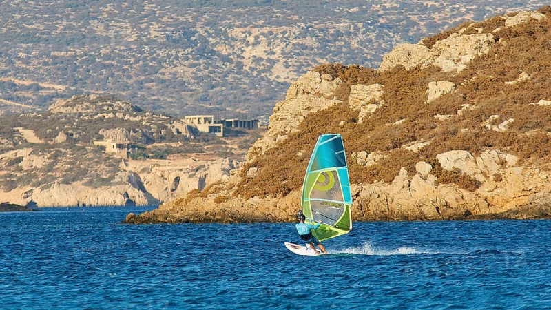 Person windsurfing along a rocky coast on blue water, windsurfer, Meltemi windsurfing spot, Devils Bay, Paralia Vatha, Vatha Beach, southeast coast, Karpathos, Dodecanese, Greek Islands, Greece, Europe