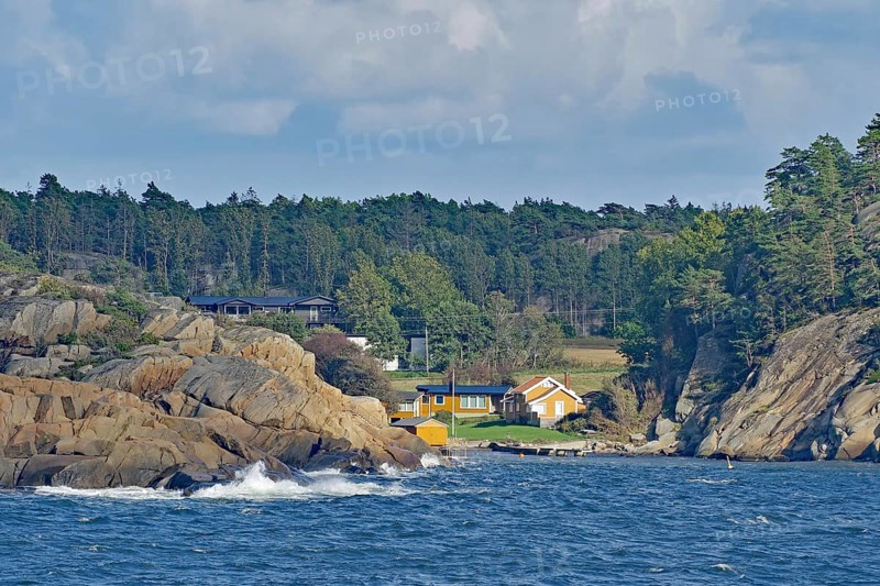 Coastal view with a wooded hill, rocks on the shore, several houses and waves under a cloudy sky, Holiday homes, Archipelago, Sandefjord, Norway, Europe