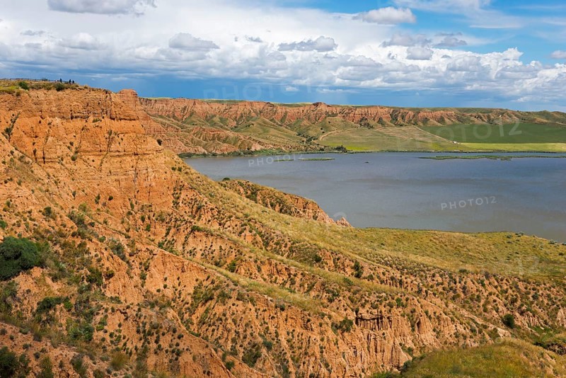 Ein felsiger Canyon, der sich entlang eines Sees erstreckt, unter einem überwiegend blauen Himmel mit Wolken, Barrancas de Burujón, Burujon, río Tajo, Fluss Tajo, embalse de Castrejón, Stausee de Castrejon, Toledo, Kastilien-La Mancha, Spanien