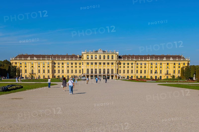 Schönbrunn Palace with yellow facade and blue sky in the background, some tourists in the foreground, Vienna, Austria, Europe